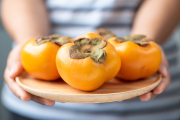 Ripe persimmon fruit on wooden plate holding by woman hand