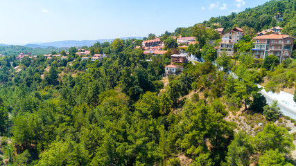 Fototapeta na wymiar Aerial view of Pano Platres village,winter resort, on Troodos mountains, Limassol, Cyprus. Bird's eye view of pine tree forest, red roof tiled houses, hotels, panagias faneromenis church from above.