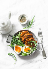 Healthy breakfast - sweet potato fritters, boiled egg, arugula salad on light background, top view