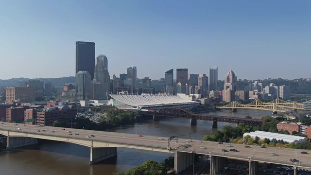 A hazy morning cinematic aerial establishing shot of the Pittsburgh skyline. Traffic passes on the Veterans Bridge over the Allegheny River in the foreground.  	