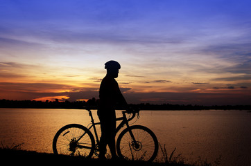 Silhouette of the man on a bicycle, with beautiful lake near by at sunset