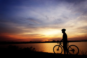 Fototapeta na wymiar Silhouette of the man on a bicycle, with beautiful lake near by at sunset