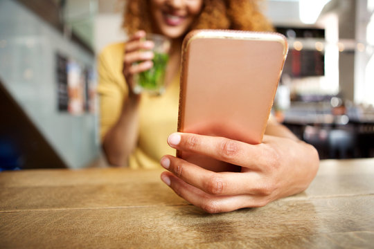 front portrait of happy young woman sitting at cafe with a drink, looking at mobile phone