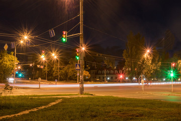 Car intersection with traffic lights and passing cars at night with long exposure.