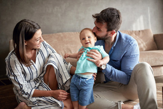 Proud Parents Mother And Father Kissing Little Cute Baby At Home.