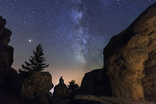 Man sitting under the stars Milky Way in the mountains silhouette rock.