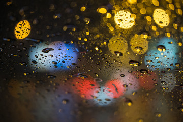 Rain drops rain on the window with blurred traffic light