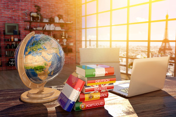 Languages learning and translate, communication and travel concept, books with covers in colors of flags of Europe countries, laptop and globe on a table in a modern interior