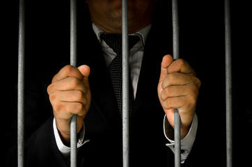 Close-up Of Businessman Hand Holding Metal Bars In Jail with dark environments.
