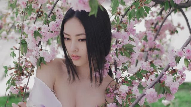 Backstage of outdoor photoshoot of beautiful young asian woman surrounded by flowers on spring. Perfect model with creative vivid makeup and pink lipstick on lips and traditional japanese hairstyle