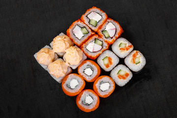 Set of sushi, rolls, uramaki, hosomaki, california, philadelphia, lava sauce, tobiko caviar, raw seafood, soy sauce, marinated ginger and wasabi, black isolated background view from above For the menu