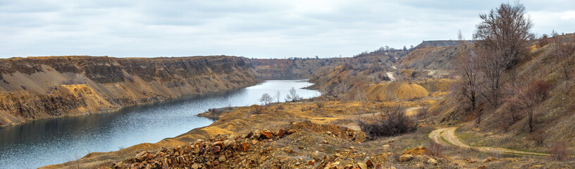 The panoramic view of industrial scene with flooded quarry and heaps of boulders