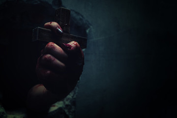 Horror Scene with Bloody Hand is holding a holy cross.