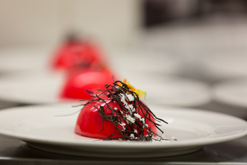 A red icecream desert topped with a decorative chocolate finish prepared by a gourmet chef.