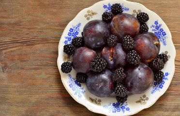 Fresh dark fruits and berries on a plate, top view, copy space