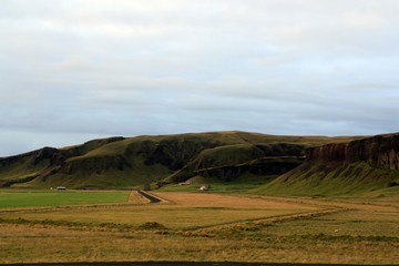 Carretera rural en el campo islandés. Granja con pastizales cercados y ovejas rodeado de colinas volcánicas.