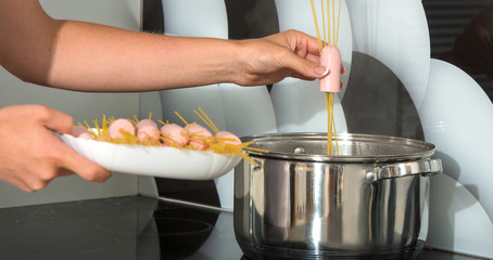 A woman is cooking spaghetti and sausages.	
