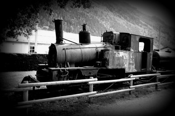 Old rusty steam locomotive in the open air in a parking lot in Chamonix. French Alps. Black and white photo. Old style of postcard.