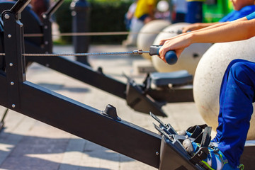 The young boy make exercises on rower mashine in the park in summertime