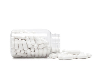 white medicine capsules spill out from bottle