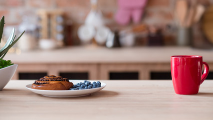 healthy eating and morning food. quick and easy breakfast. pastry poppy seed bun and fresh blueberry. tea or coffee in a red mug on a kitchen table.