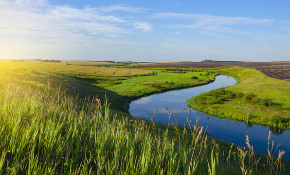 Fototapeta Beautiful view of river curve,green and yellow fields illuminated by the warm light of rising sun.