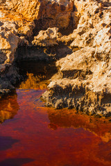 Volcanic stone coast in Cyprus with red water