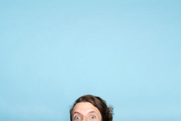 startled eccentric whimsical man with smiling eyes peeping out from the bottom of blue background....