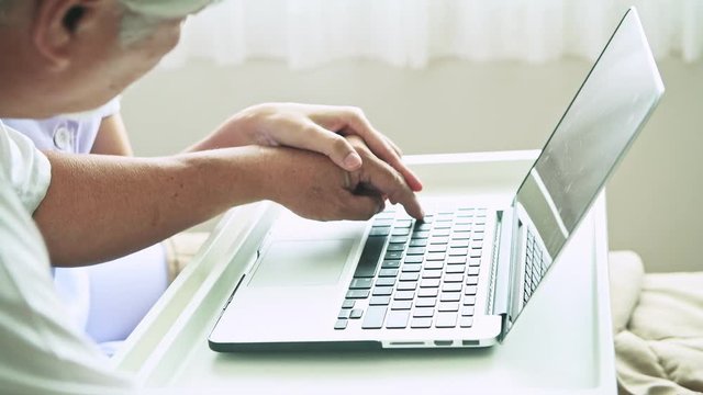 Young beautiful female nurse teaching computer skill to senior man. Asian woman using laptop with old asian man with white beard in bed. Senior home service, care taker concept.