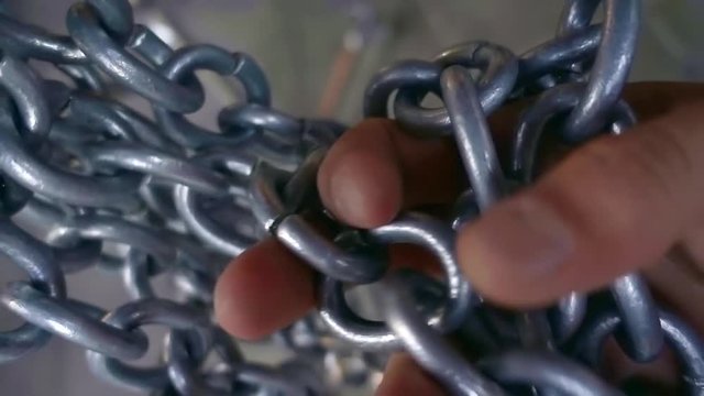 man rough hand touches the links of the steel chain close-up