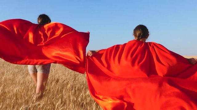 Teenage girl superheroes runs across field with wheat against blue sky.