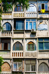 Colourful and oddly shaped arched and rectangular windows on the facade of an old Soviet-era concrete apartment building in Bishkek