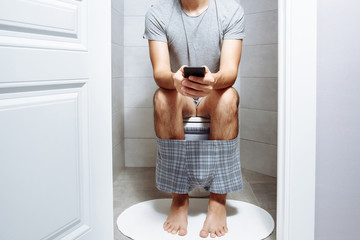 Man with smartphone sitting on the toilet