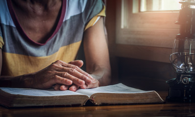 focus on a hands of old woman while praying on Bible