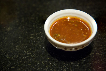 Chinese sukiyaki sauce in little bowl on black floor. sauce for dipping meat and vegetable. Chinese sauce for adding flavor to sukiyaki and shabu shabu.