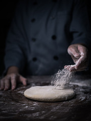 pastry chef hand sprinkling white flour over Raw Dough on kitchen table.