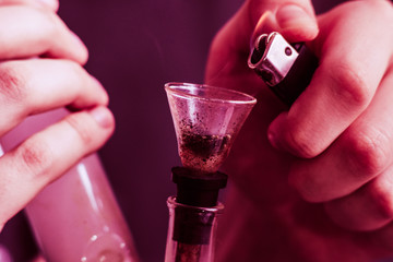 Bong lighter for A man smokes cannabis weed, in his hands. Smoke on a black background. Concepts of...