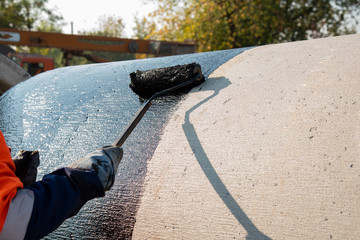 Roofer worker painting black coal tar or bitumen at concrete