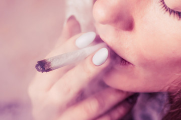 A woman smokes cannabis weed, a joint and a lighter in his hands. Smoke on a black background....