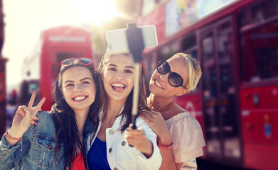 summer vacation, holidays, travel, technology and people concept- group of smiling young women taking picture with smartphone on selfie stick over london city street background