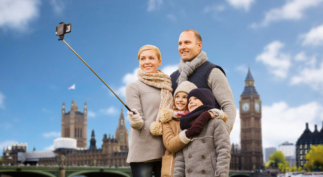family, travel and tourism concept - happy mother, father, daughter and son taking picture by smartphone on selfie stick over big ben tower in london city background