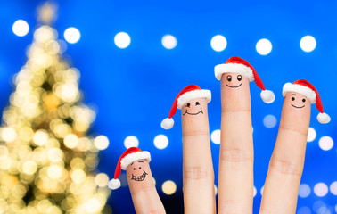 Naklejka premium holidays and body parts concept - close up of four fingers with santa hats over christmas tree lights background