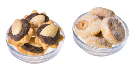 Two glass bowls of Christmas sweets. Sweet baked pastries close-up. Pile of shortbread cookies with hazelnuts. Coconut cupcakes filled by chocolate, decorated by almond. Isolated on white background.
