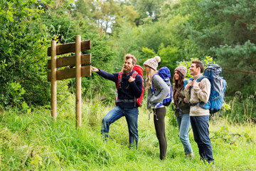 travel, tourism, hiking and people concept - group of happy friends or travelers with backpacks looking at signpost © Syda Productions