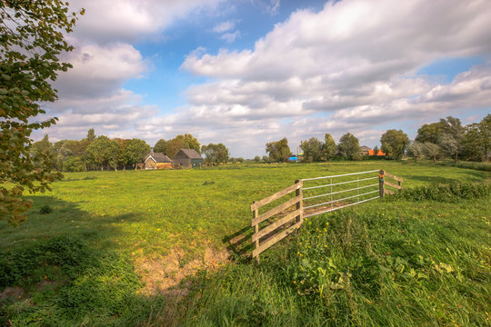 A large fence for a beautiful green meadow of a farm with a beautiful cloudy sky.