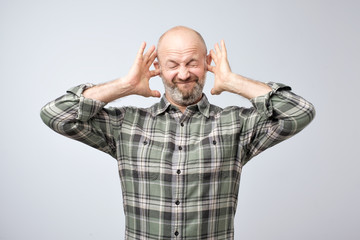 Annoyed mature man plugging ears with fingers