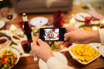 food, technology and holidays concept - close up of male hands photographing roast turkey by smartphone at christmas dinner