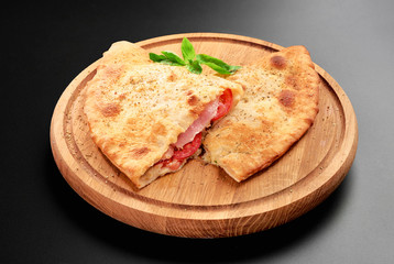 Pizza calzone with basil leaves close up on wooden round board cutted with tomato cheese and ham isolated