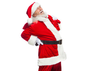 Christmas. Santa Claus is suffering from back pain and holds a red bag with gifts on his back. Isolated on white background.