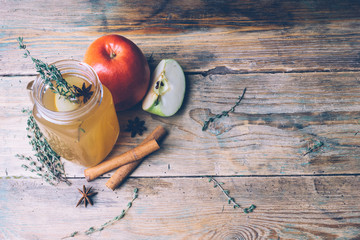 Apple cider (mulled cider) with cinnamon sticks and fresh apples on wooden background. Autumn...